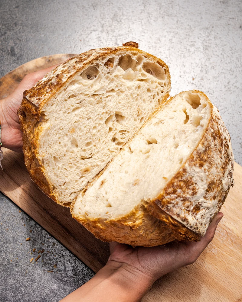 Close-up of freshly baked sourdough bread held by a baker, showcasing its texture and crust.